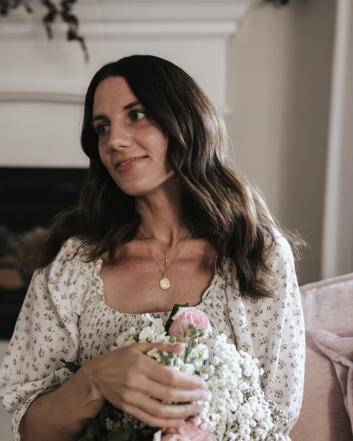 Gold filled Miraculous Medal and crucifix necklace worn with a floral blouse, holding pink roses and baby's breath